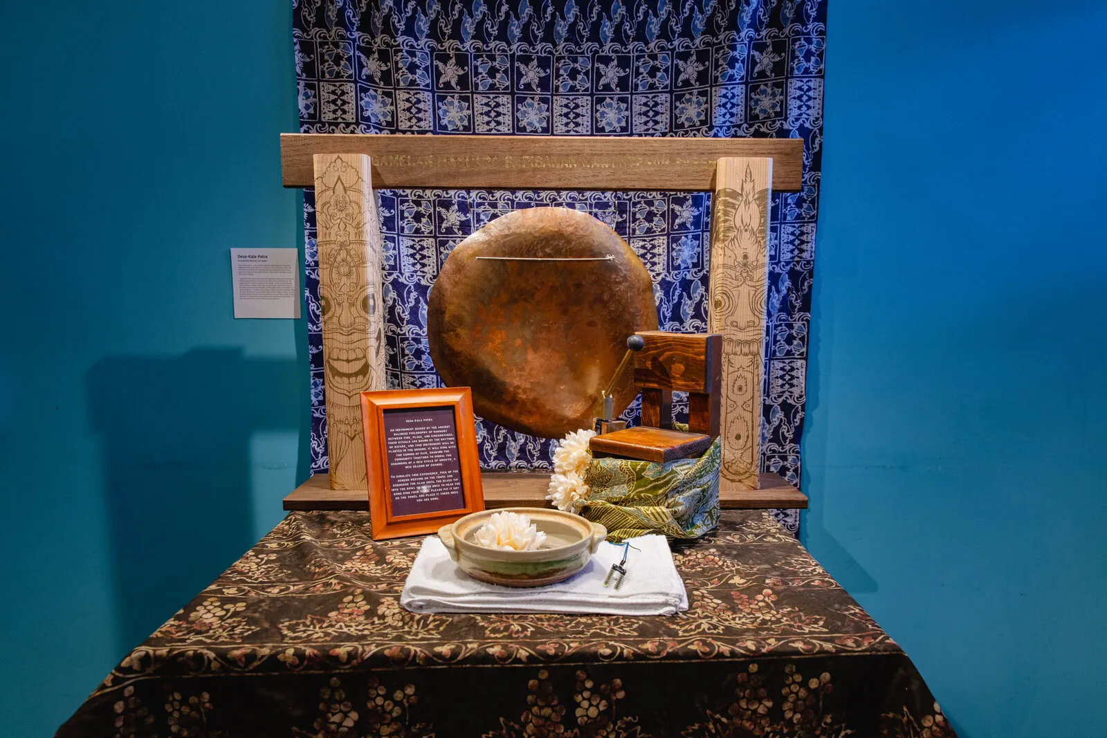 The Lagu Hantu altar — a suspended gong over an offering bowl against blue batik